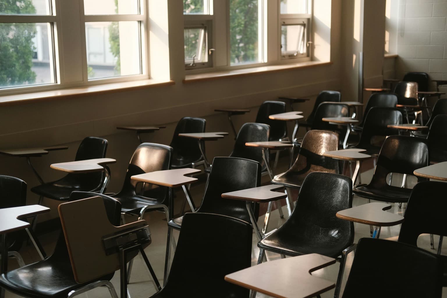 An empty classroom of desks and chairs beside a row of windows