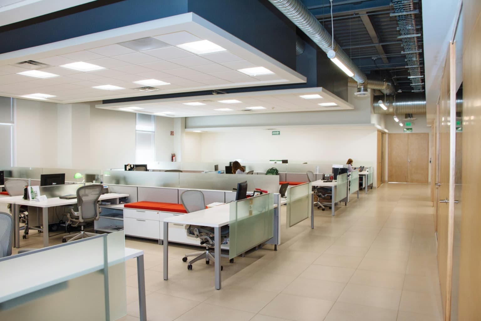 An open plan office with rows of desks and a few people working at a distance